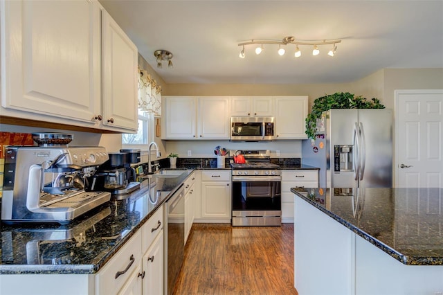 kitchen with dark wood-type flooring, a sink, white cabinetry, stainless steel appliances, and dark stone counters