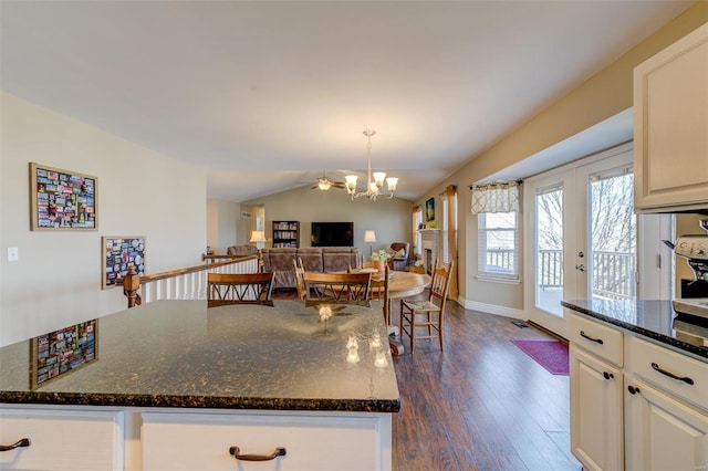 kitchen with a notable chandelier, a kitchen island, dark wood-style floors, dark stone counters, and lofted ceiling