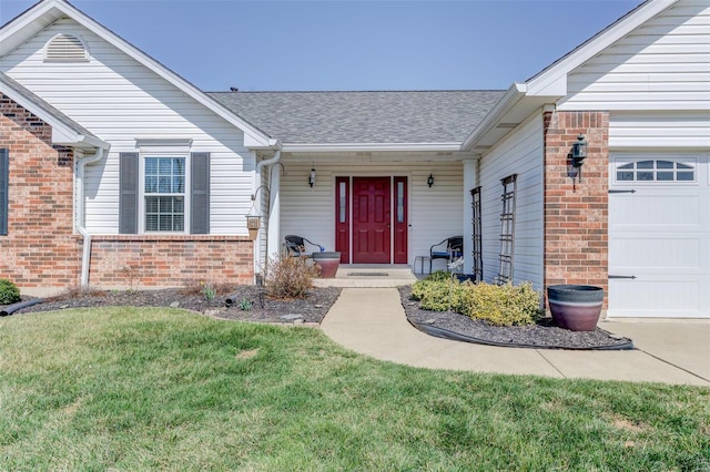 view of exterior entry with a garage, brick siding, a yard, and a shingled roof