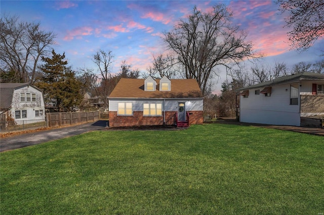 back of house at dusk with aphalt driveway, a yard, fence, and brick siding