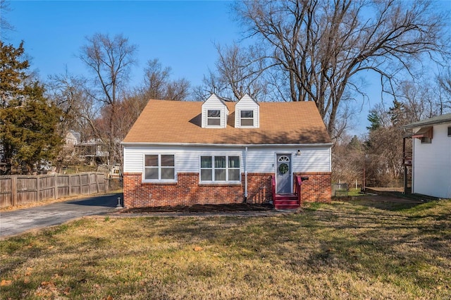 new england style home with fence, entry steps, a front lawn, aphalt driveway, and brick siding