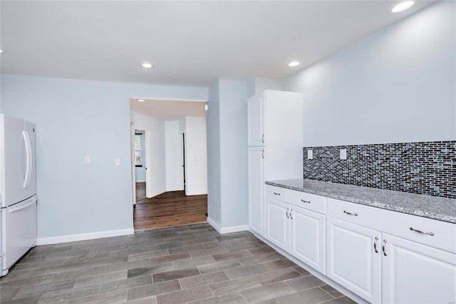 kitchen featuring light stone counters, tasteful backsplash, white cabinetry, recessed lighting, and freestanding refrigerator