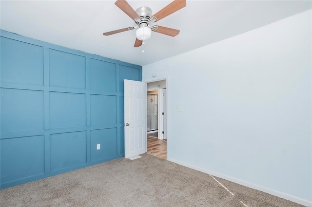 unfurnished bedroom with a decorative wall, ceiling fan, baseboards, and carpet