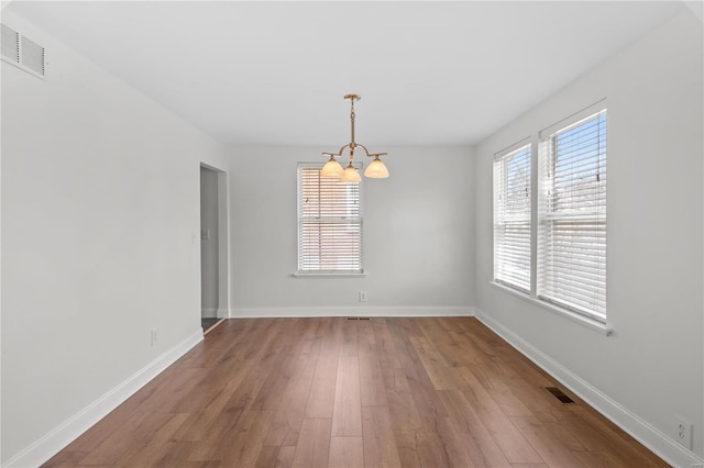 unfurnished room with a notable chandelier, baseboards, visible vents, and wood finished floors