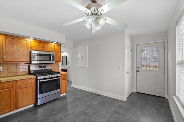 kitchen with tile countertops, baseboards, ceiling fan, decorative backsplash, and appliances with stainless steel finishes