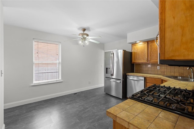 kitchen with a sink, tile countertops, stainless steel appliances, decorative backsplash, and baseboards