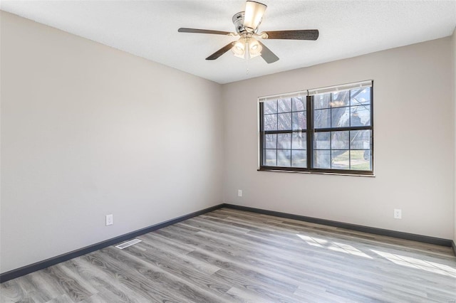 spare room featuring visible vents, ceiling fan, baseboards, wood finished floors, and a textured ceiling