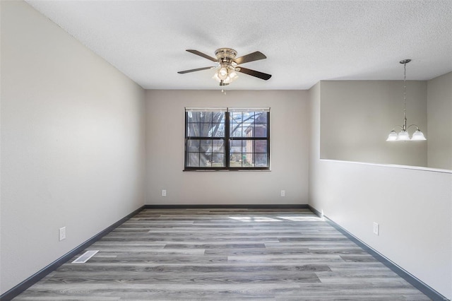 spare room featuring visible vents, a textured ceiling, wood finished floors, and ceiling fan with notable chandelier