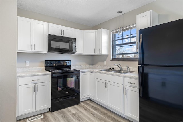 kitchen featuring visible vents, a sink, black appliances, white cabinets, and light countertops