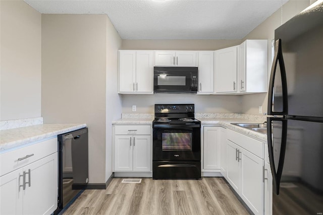 kitchen with white cabinetry, black appliances, light wood-type flooring, and a textured ceiling