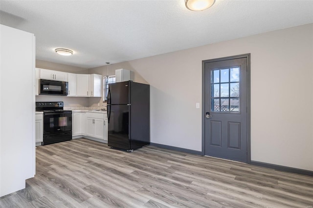 kitchen featuring light wood finished floors, black appliances, baseboards, light countertops, and white cabinetry