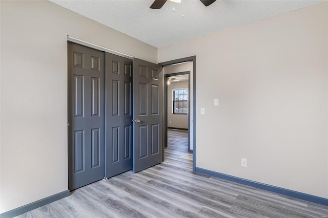 unfurnished bedroom with a closet, light wood-style flooring, a textured ceiling, and baseboards