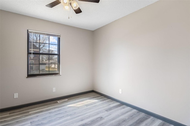 spare room featuring visible vents, a textured ceiling, wood finished floors, baseboards, and ceiling fan