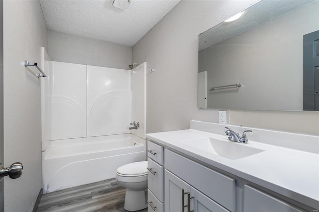 full bath featuring toilet, a textured ceiling, wood finished floors, washtub / shower combination, and vanity