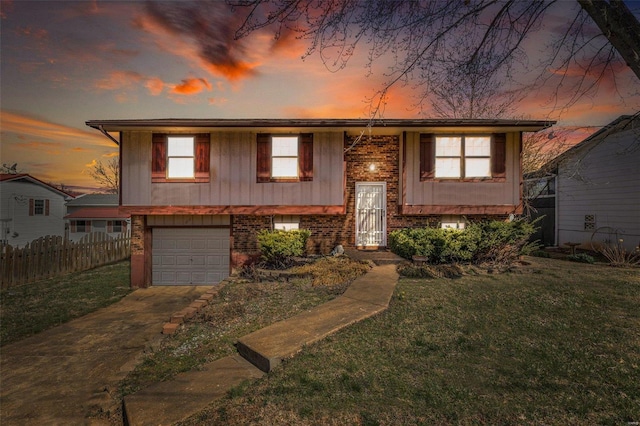 raised ranch with brick siding, an attached garage, fence, a lawn, and driveway