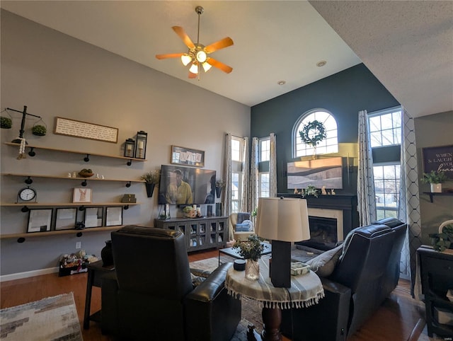 living area featuring a glass covered fireplace, baseboards, wood finished floors, and ceiling fan