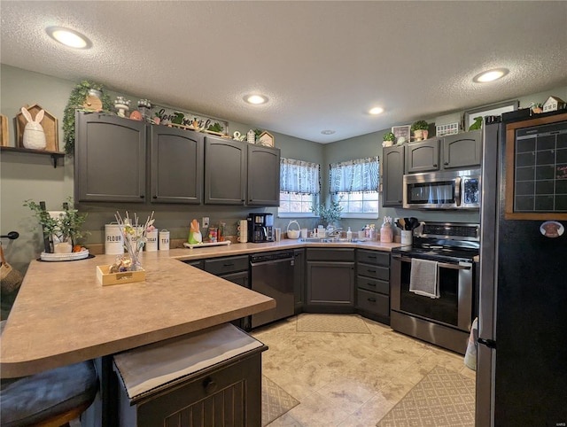 kitchen featuring a textured ceiling, a peninsula, appliances with stainless steel finishes, and gray cabinetry