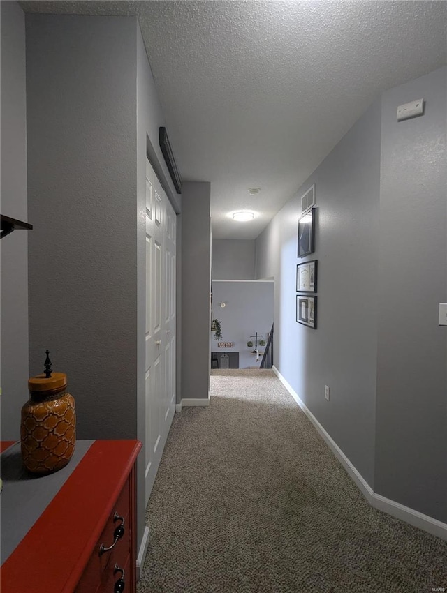 hall with visible vents, baseboards, carpet, and a textured ceiling