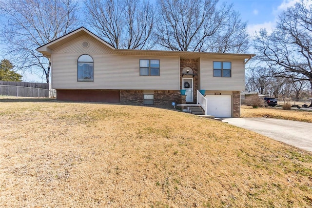 bi-level home featuring a garage, concrete driveway, a front lawn, and fence