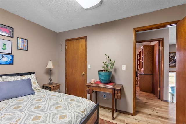 bedroom with light wood-style flooring, baseboards, and a textured ceiling