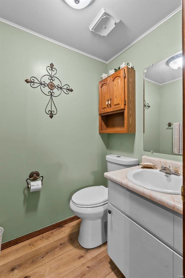 bathroom featuring vanity, wood finished floors, baseboards, ornamental molding, and toilet