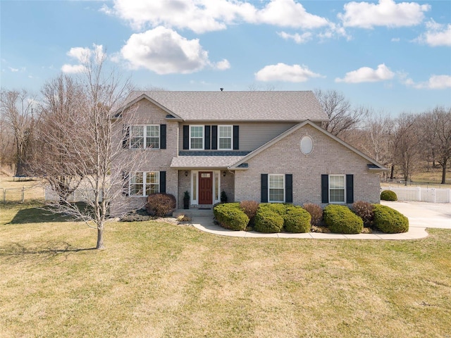 view of front of property with a front yard, fence, brick siding, and a shingled roof