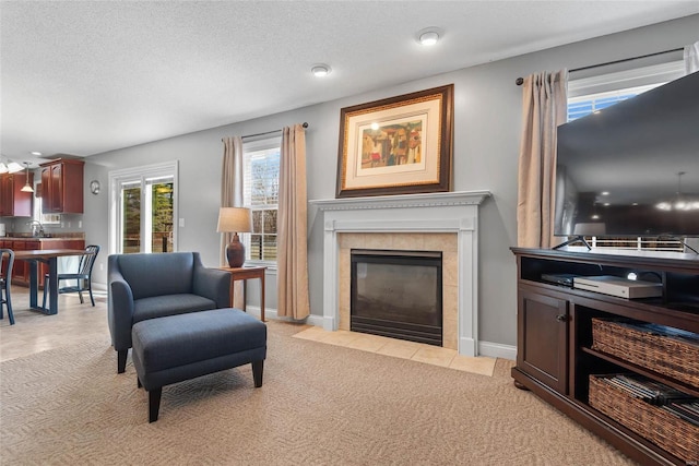 living room with baseboards, light carpet, a textured ceiling, and a tile fireplace