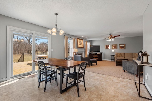 dining space with visible vents, ceiling fan with notable chandelier, a textured ceiling, a fireplace, and baseboards