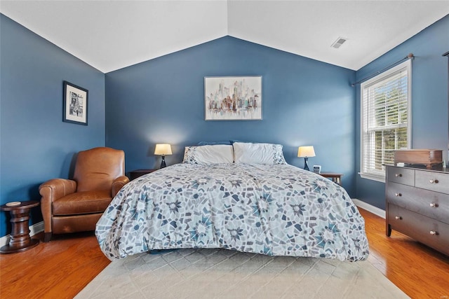 bedroom with vaulted ceiling, wood finished floors, visible vents, and baseboards