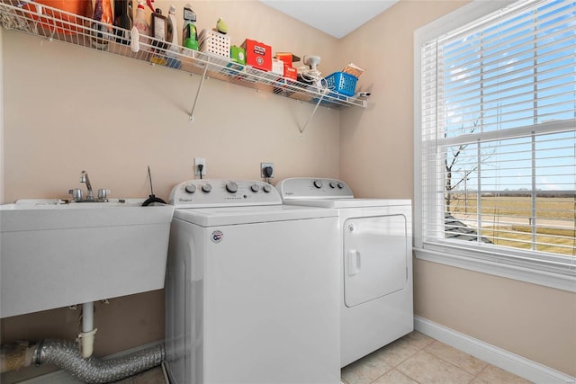 washroom featuring a sink, light tile patterned flooring, baseboards, laundry area, and washing machine and clothes dryer