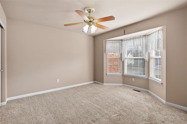 carpeted spare room featuring visible vents, ceiling fan, and baseboards