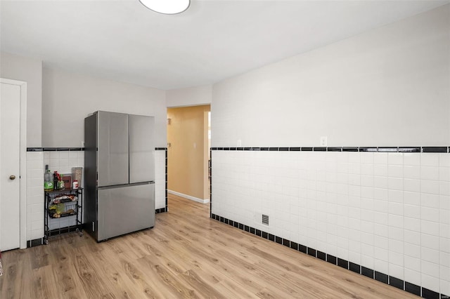 kitchen featuring light wood-type flooring, tile walls, a wainscoted wall, and freestanding refrigerator