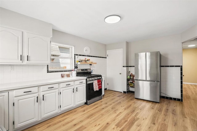 kitchen featuring light wood-style flooring, white cabinetry, stainless steel appliances, tile walls, and light countertops