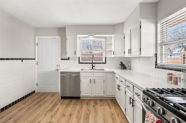 kitchen featuring light wood finished floors, a sink, stainless steel appliances, light countertops, and white cabinets