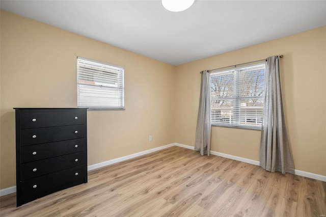 unfurnished bedroom featuring multiple windows, baseboards, and light wood finished floors