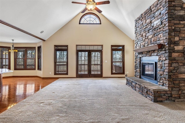 unfurnished living room with high vaulted ceiling, ceiling fan with notable chandelier, wood finished floors, a fireplace, and baseboards