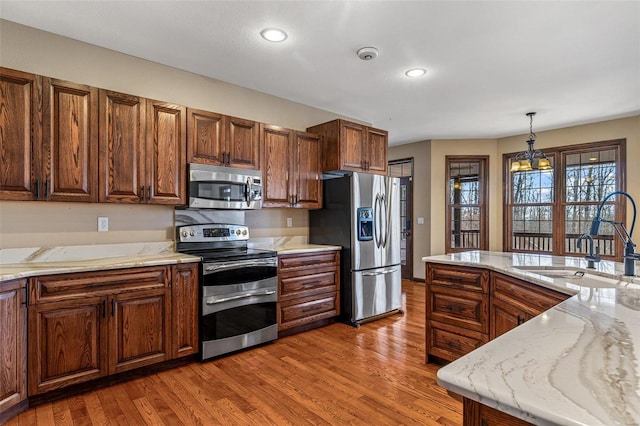 kitchen with hanging light fixtures, light wood-style flooring, stainless steel appliances, and a sink