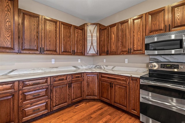 kitchen featuring visible vents, dark wood-type flooring, light stone counters, appliances with stainless steel finishes, and brown cabinetry