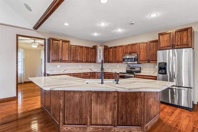 kitchen with a sink, dark wood-type flooring, light stone counters, and stainless steel appliances