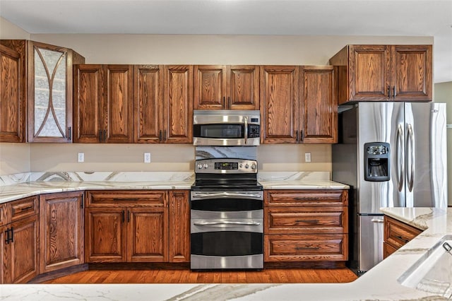 kitchen with light stone counters, brown cabinets, dark wood finished floors, and stainless steel appliances