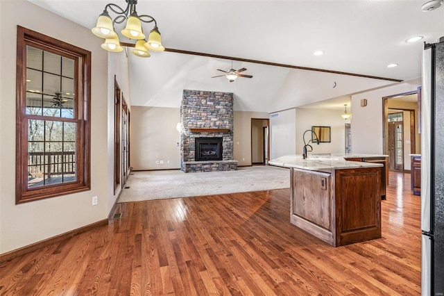 kitchen featuring an island with sink, lofted ceiling, ceiling fan with notable chandelier, a fireplace, and wood finished floors