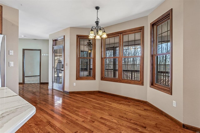 unfurnished dining area with baseboards, a notable chandelier, and light wood finished floors