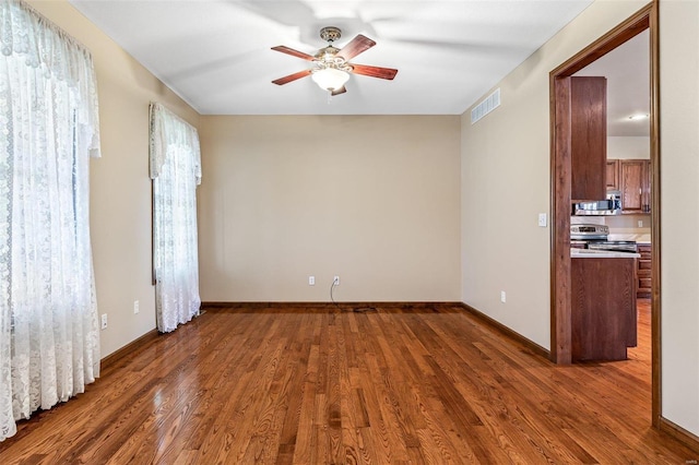 empty room with baseboards, dark wood-style floors, visible vents, and ceiling fan