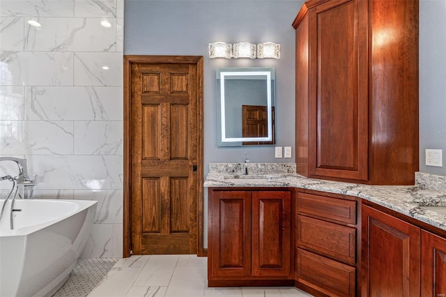 full bathroom featuring a sink, a freestanding bath, marble finish floor, and double vanity