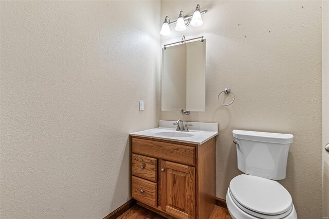 half bath with vanity, toilet, wood finished floors, and baseboards