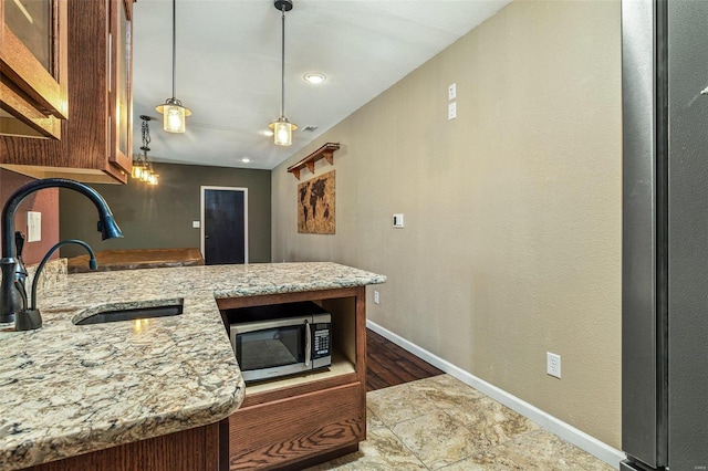 kitchen featuring baseboards, a peninsula, a sink, hanging light fixtures, and stainless steel microwave