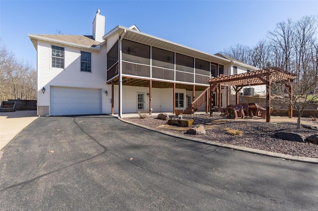 rear view of property featuring ceiling fan, aphalt driveway, a chimney, a garage, and a sunroom