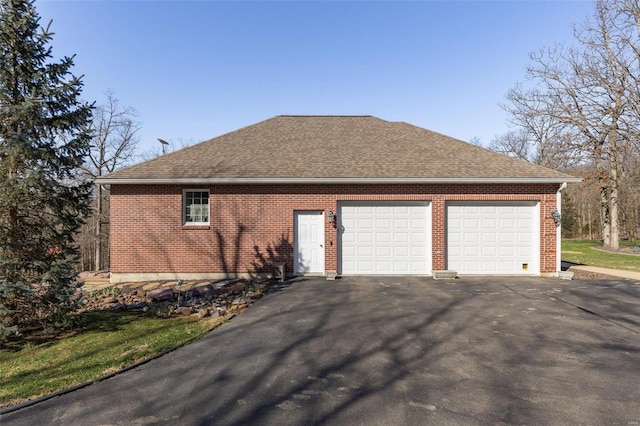 view of side of home with brick siding, a garage, driveway, and a shingled roof