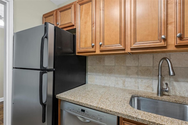 kitchen with light stone countertops, a sink, brown cabinetry, stainless steel appliances, and backsplash