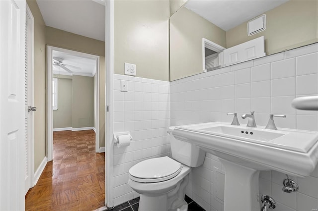 half bathroom featuring tile walls, baseboards, a ceiling fan, and toilet